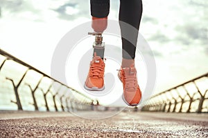 Never give up Cropped photo of disabled woman with prosthetic leg in sportswear jumping on the bridge