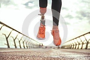 Never give up Cropped photo of disabled woman with prosthetic leg in sportswear jumping on the bridge photo