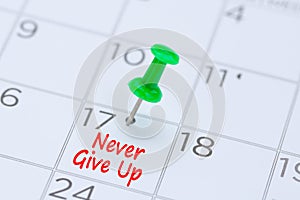 Never give up written on a calendar with a green push pin to re