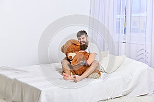 Never grow up concept. Guy on happy face hugs giant teddy bear. Macho with beard and mustache cuddling with plush toy