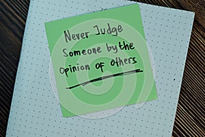 Never judge someone by the opinion of others write on sticky notes isolated on Wooden Table. Motivation concept