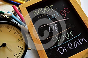 Never let go of your dream on phrase colorful handwritten on chalkboard, alarm clock with motivation and education concepts