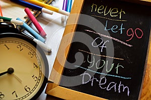 Never let go of your dream on phrase colorful handwritten on chalkboard, alarm clock with motivation and education concepts