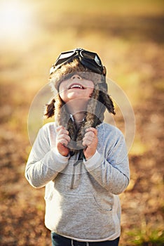 Never let go of your dreams. a cute little boy wearing a pilots hat and goggles while playing outside.