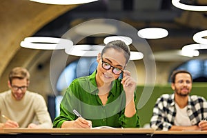 Never stop learning. Focused asian woman wearing eyeglasses making some notes while studying with colleagues during