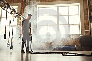 Never stop. Side view of young athletic man with perfect body doing crossfit exercises with a rope in the gym.