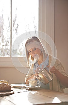 Never underestimate the power of a good cup of tea. A beautiful young woman pouring herself a cup of tea while sitting