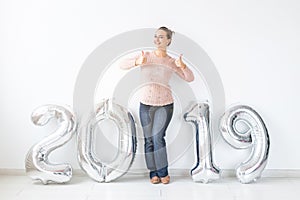 New 2019 Year is coming concept - Happy woman showing thumbs up near silver colored numbers indoors.