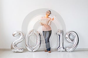 New 2019 Year is coming concept - Happy woman standing near silver colored numbers and sparklers indoors.