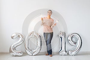 New 2019 Year is coming concept - Happy woman standing near silver colored numbers and sparklers indoors.