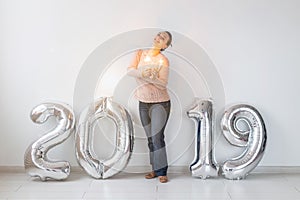 New 2019 Year is coming concept - Happy woman standing near silver colored numbers and sparklers indoors.