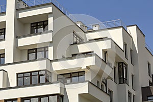 New apartment building with terraced balconies, shiny windows and low protective fence on flat roof.