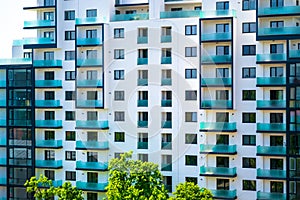 New apartments building with empty flats, white exterior with blue-green glass windows and a few green trees at the bottom.