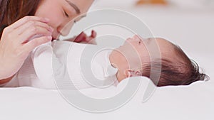 New asian mom playing to adorable newborn baby on bed smiling and happiness at home.Mom talking with infant baby and holding her