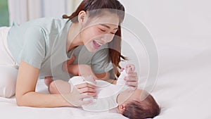 New asian mom playing to adorable newborn baby on bed smiling and happiness at home.Mom talking with infant baby and holding her