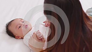 New asian mom playing to adorable newborn baby on bed smiling and happiness at home.Mom talking with infant baby and holding her