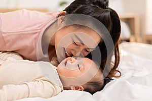 New asian mom playing to adorable newborn baby on bed smiling and happiness at home.Mom talking with infant baby and kissing on