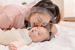 New asian mom playing to adorable newborn baby on bed smiling and happiness at home.Mom talking with infant baby and kissing on