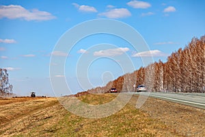 A new asphalt gray road with a white dividing strip between the forest and the field covered with grass in Russia with car driving