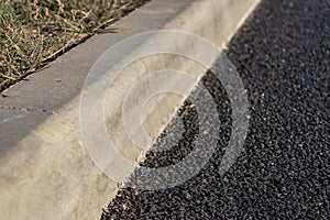 New asphalt on the road is laid along the concrete curb. Close-up. Road repair