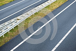 New asphalt road with with lines on both sides going to the right. Two drive lanes with guardrail in the middle. Travel road trip