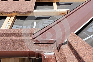 New asphalt shingle roof with brown rain gutter, wooden beams and vapour control layer.