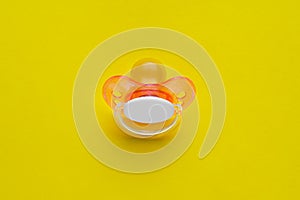 New baby pacifier on yellow background, top view