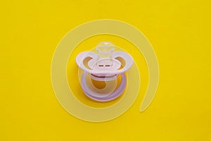 New baby pacifier on yellow background, top view