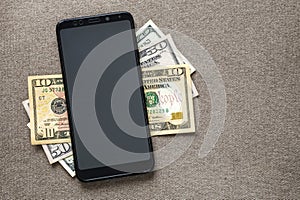 New black modern cellphone on money dollars banknotes background. Modern technology, communication and online trade using gadget