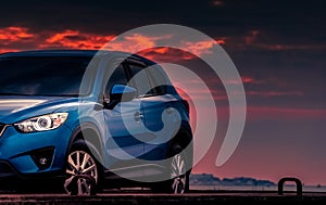New blue SUV car with sport and luxury design parked on concrete road by the sea at sunset with dramatic sky and clouds.Automotive