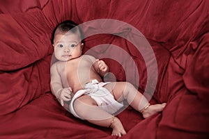 New born is 3 months old. Newborn is laying on the red chairs. Infant is Asian person.