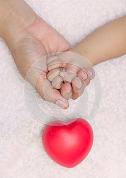 New born baby hand in mom palm with red heart