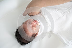 New born baby smiling while mother`s hand swaddling her body with white blanket.