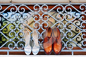 New brown men`s shoes with women`s white sandals on the window at the metal grille outside.