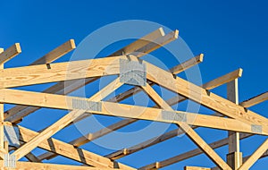 A new build roof with a wooden truss framework with a blue sky background.