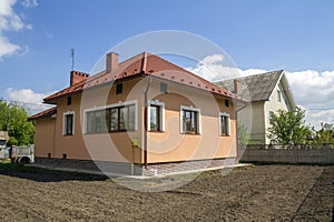 New built one-store cottage house with red tiling roof, plastic windows, plastered walls and high chimneys on fenced land plot in