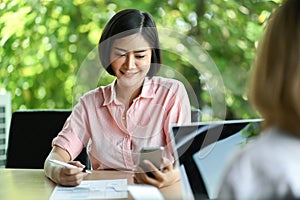 New businesswoman sitting in office using a mobile phone and smiling,Colleagues are using laptop sitting opposite