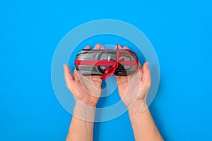 New car gift concept. Toy car model tied with a red ribbon and bow in human hands on blue background. Buy automobile, best offer,