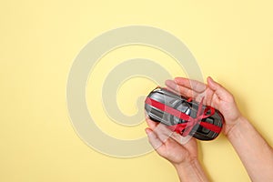 New car gift concept, Toy car with red ribbon in human hands on yellow background. Top view. Auto dealership and rental, raffle