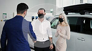 New car owners getting keys to purchased luxury auto in dealership, wearing masks