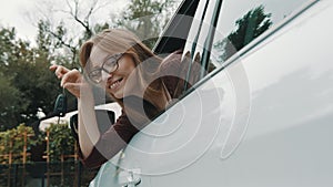 New car purchase. Young happy woman waving with the car keys through the widow of the vehicle