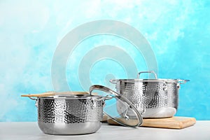 New clean saucepans on table against color background