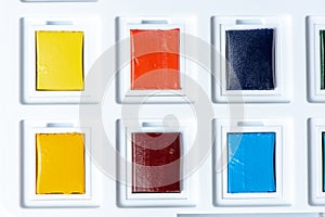 New cuvettes with watercolors in a box close-up. Yellow, orange, red and blue colors
