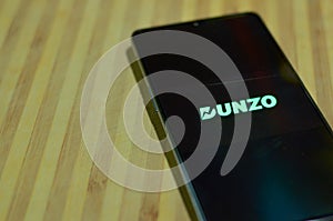 New Delhi, India, 2020. Flat lay Dunzo Delivery app logo glowing on the mobile phone screen on a wooden background. Selective