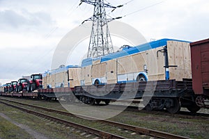 New farm tractors and trolleybus being shipped on rails. Special freight train carrying trolley-buses and agriculture tractors.