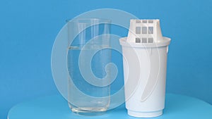 New filter cartridge for water purification and a glass of clean water rotate on a blue background close-up. Concept of