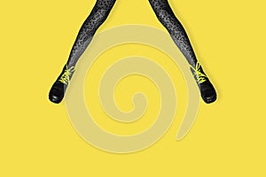 New gray female boots with bright yellow laces on long slender woman legs in gray tiger print tights isolated on yellow background