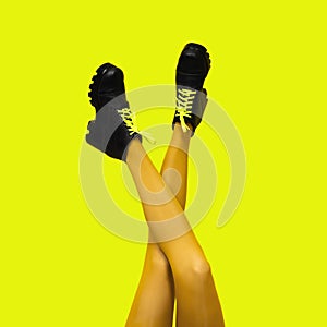 New gray female boots on long slender crossed woman legs in bright yellow tights isolated on yellow background. Pop art concept