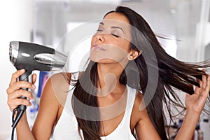 This new hairdryer makes blowdrying so easy. a beautiful young woman blow drying her hair.