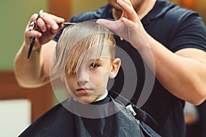 New hairstyle for young boy. Barber shop. Child getting haircut by hairdresser at the barbershop